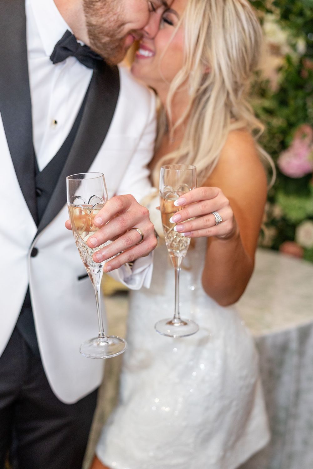 Newlyweds share a kiss while holding crystal champagne flutes at their wedding reception celebration.