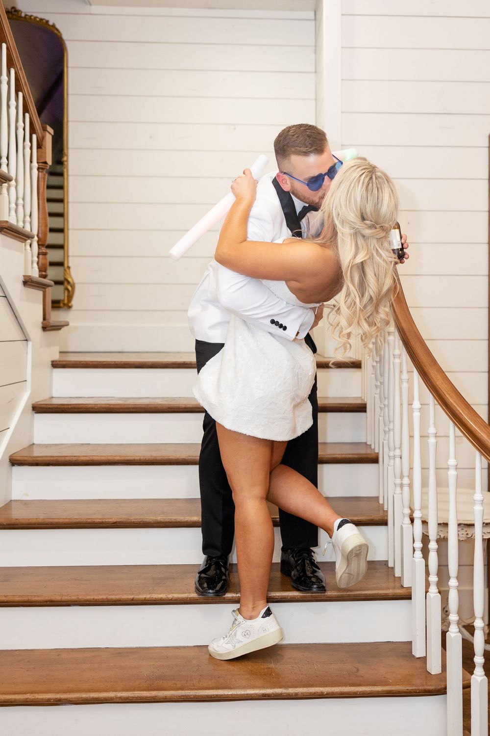 Bride and groom share romantic kiss on wooden staircase, bride in white mini dress and sneakers.