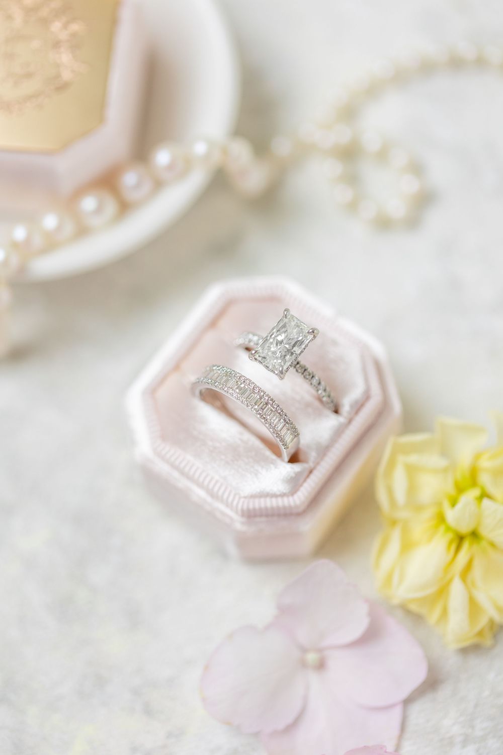 Close-up of princess cut diamond engagement ring and wedding band in pink velvet octagon ring box with floral accents.