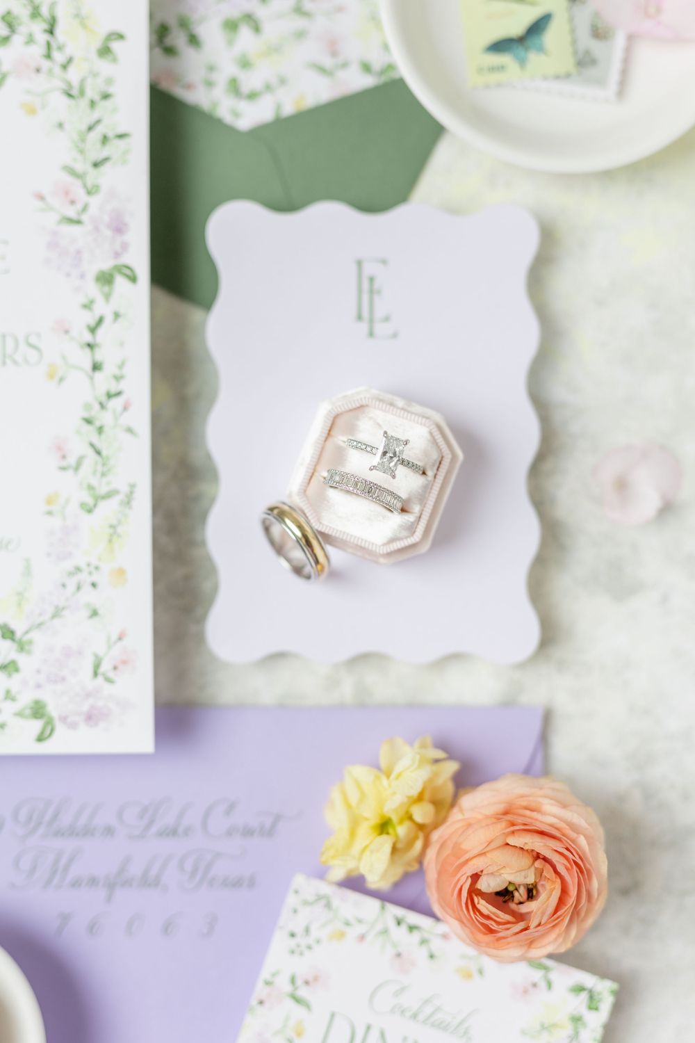Diamond engagement ring and wedding bands displayed in velvet box on wedding stationery.