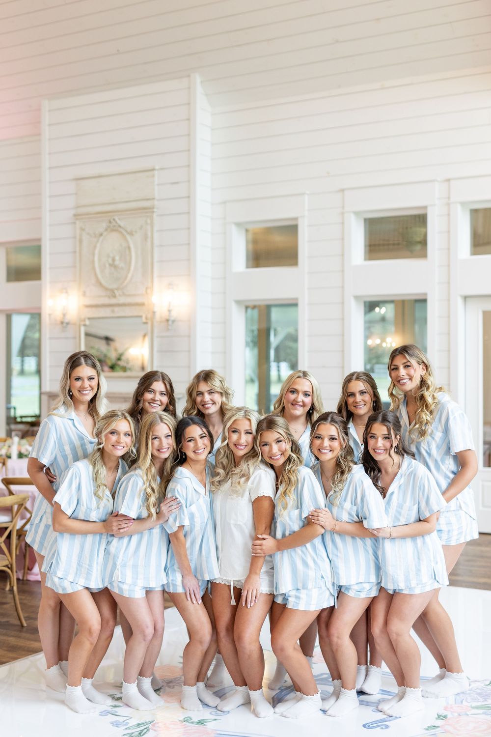 Bride and bridesmaids laughing and posing in matching blue striped pajama sets and white socks inside a bright white venue.