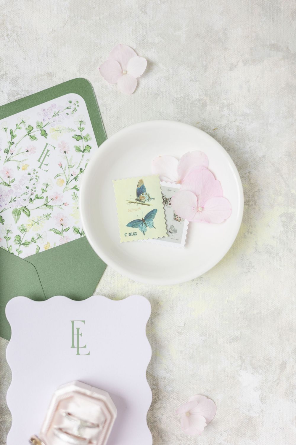 Wedding stationery flatlay with butterfly stamps, pink flowers, and green envelope liner.