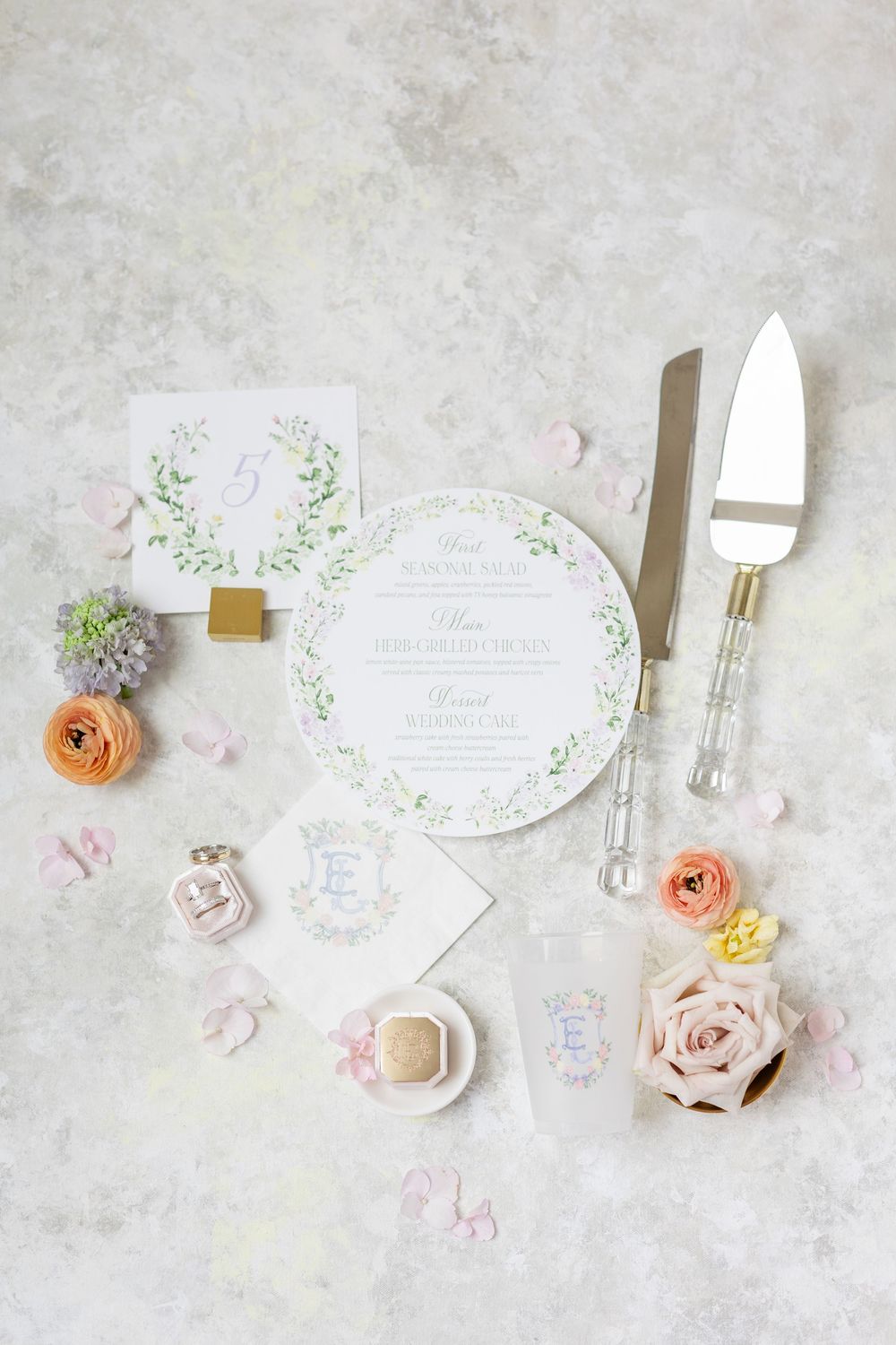 Round wedding menu card with greenery wreath design displayed with cake server and roses.