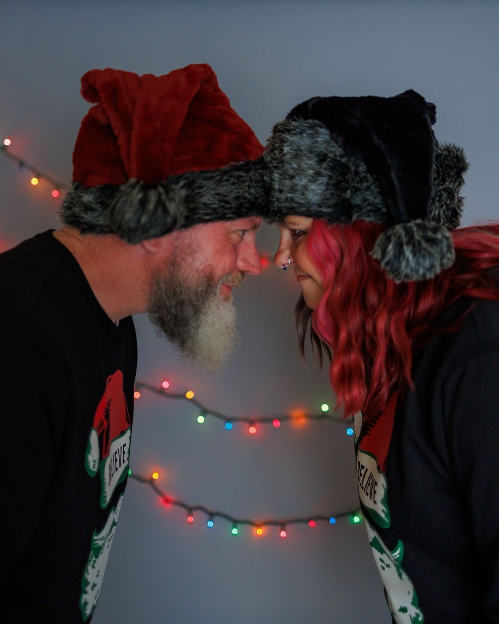 Two people in winter hats share an intimate moment as string lights twinkle behind them in the darkness.