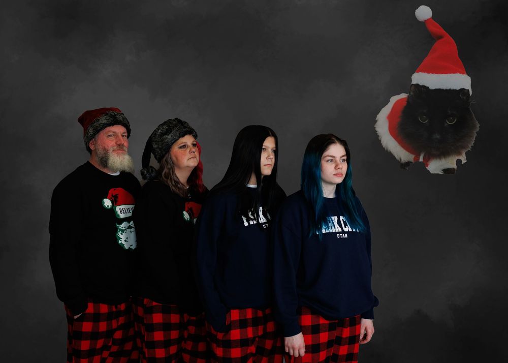 Family group wearing matching plaid pajama bottoms and blue sweaters pose together for holiday photo with Santa hat decor.