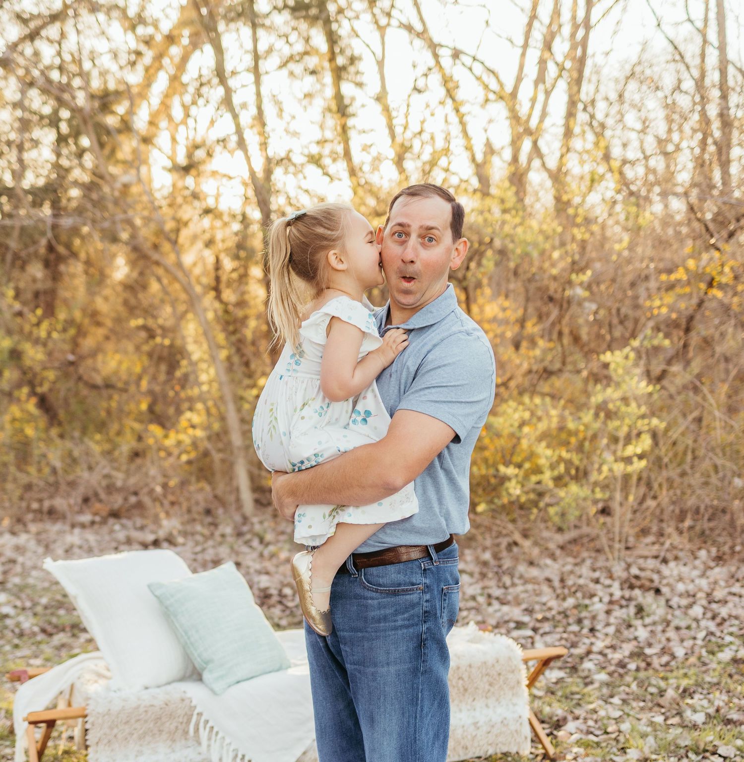 A parent and child share a tender moment outdoors at golden hour with a cozy throw blanket nearby.