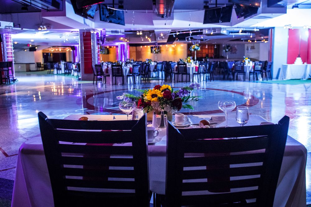 Empty tables and chairs set up in a dimly lit event space with blue ambient lighting and floral centerpieces.