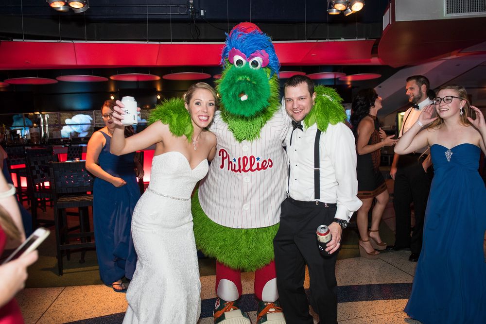 Wedding reception guests dance and celebrate at a lively party with red lighting and Philadelphia Phillies mascot Phanatic.