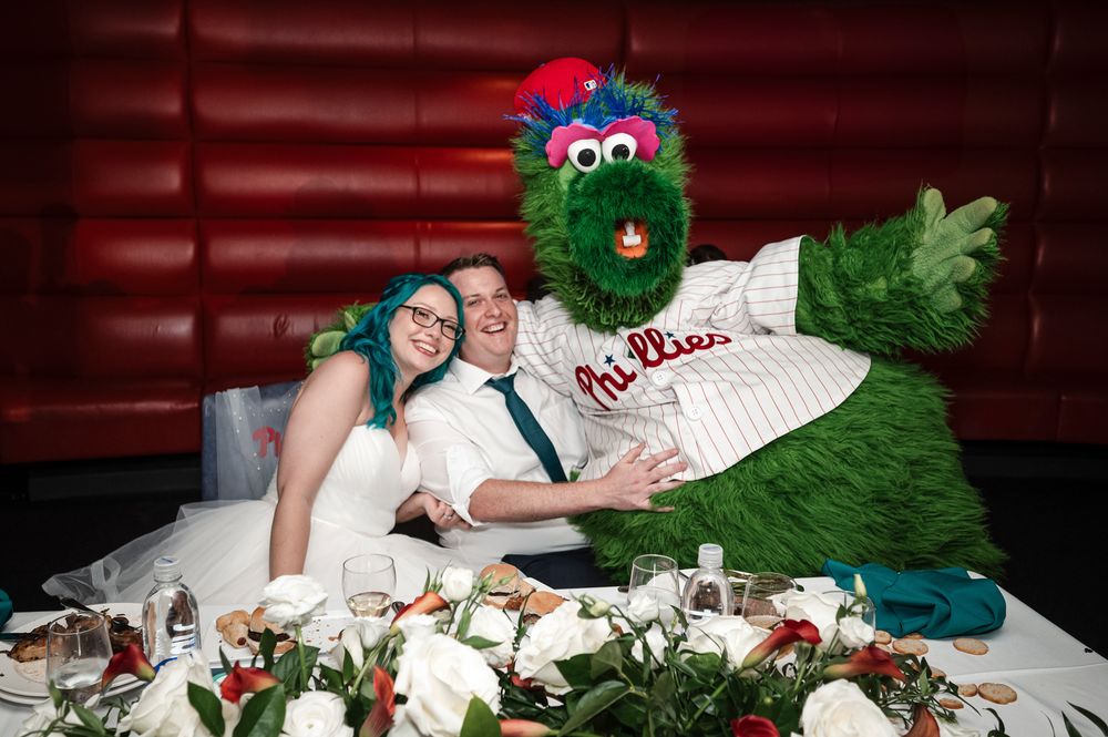 Newlyweds sit at a wedding reception table decorated with red and green holiday decor and white floral arrangements.