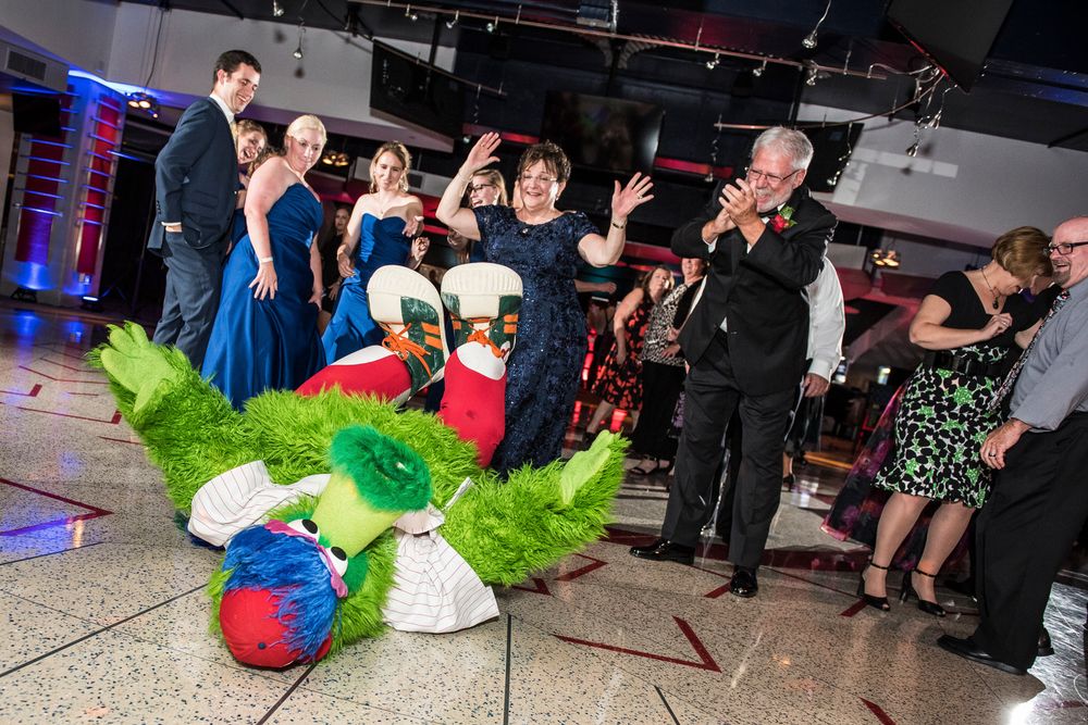 Party guests react with excitement as someone falls onto colorful decorations during a lively indoor celebration event.