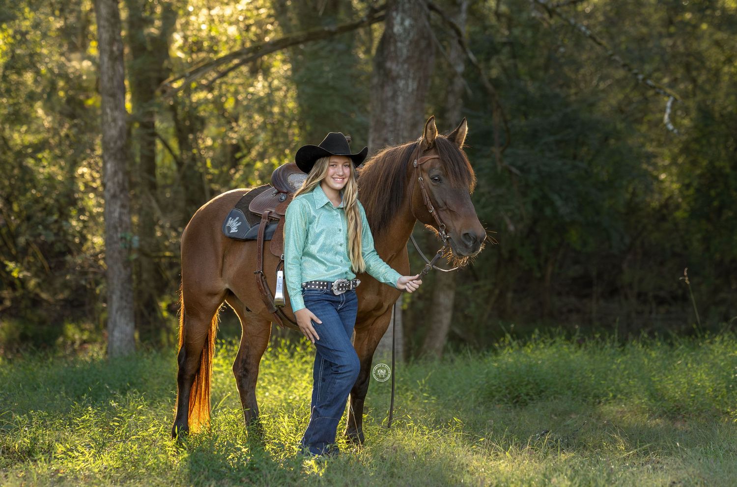 A person riding a brown horse through a sunlit forest trail in the late afternoon golden light.