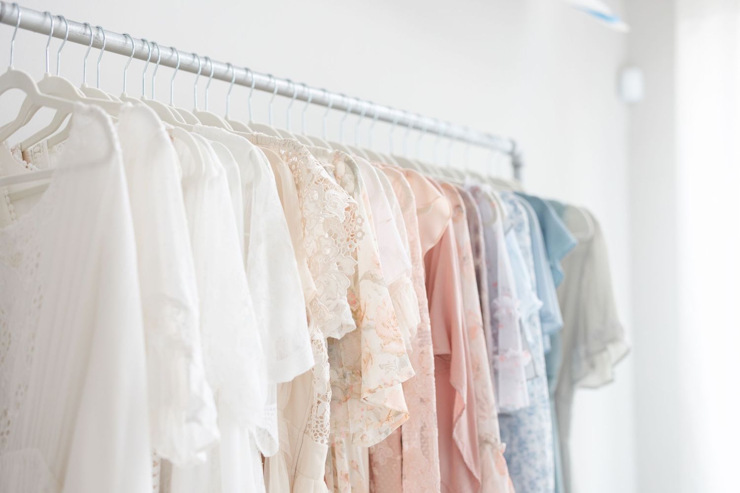 Rack of delicate pastel and white dresses hanging in bright white studio space.