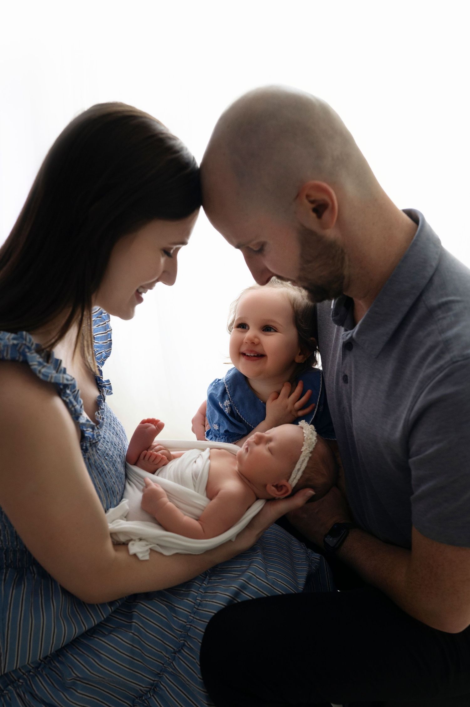 Parents holding newborn baby with older sibling during family photo session.