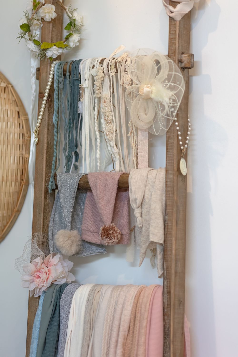 Vintage ladder displays soft pastel scarves and accessories with delicate lace and floral decorations against a white wall.