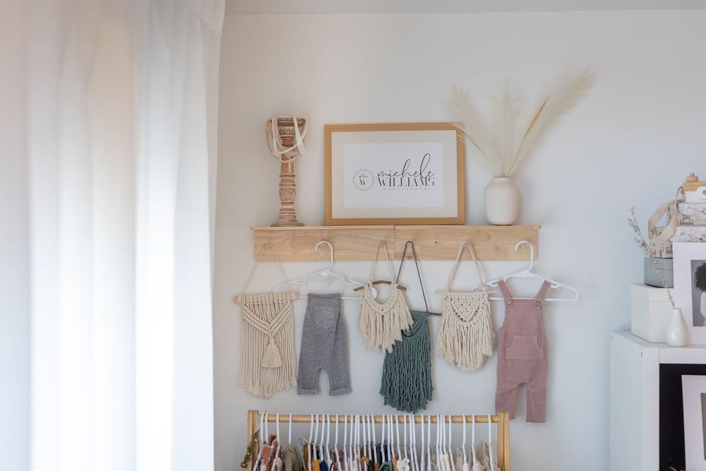 Minimalist nursery room with white walls featuring a crib, wall decor, and neutral-toned baby clothes on display.