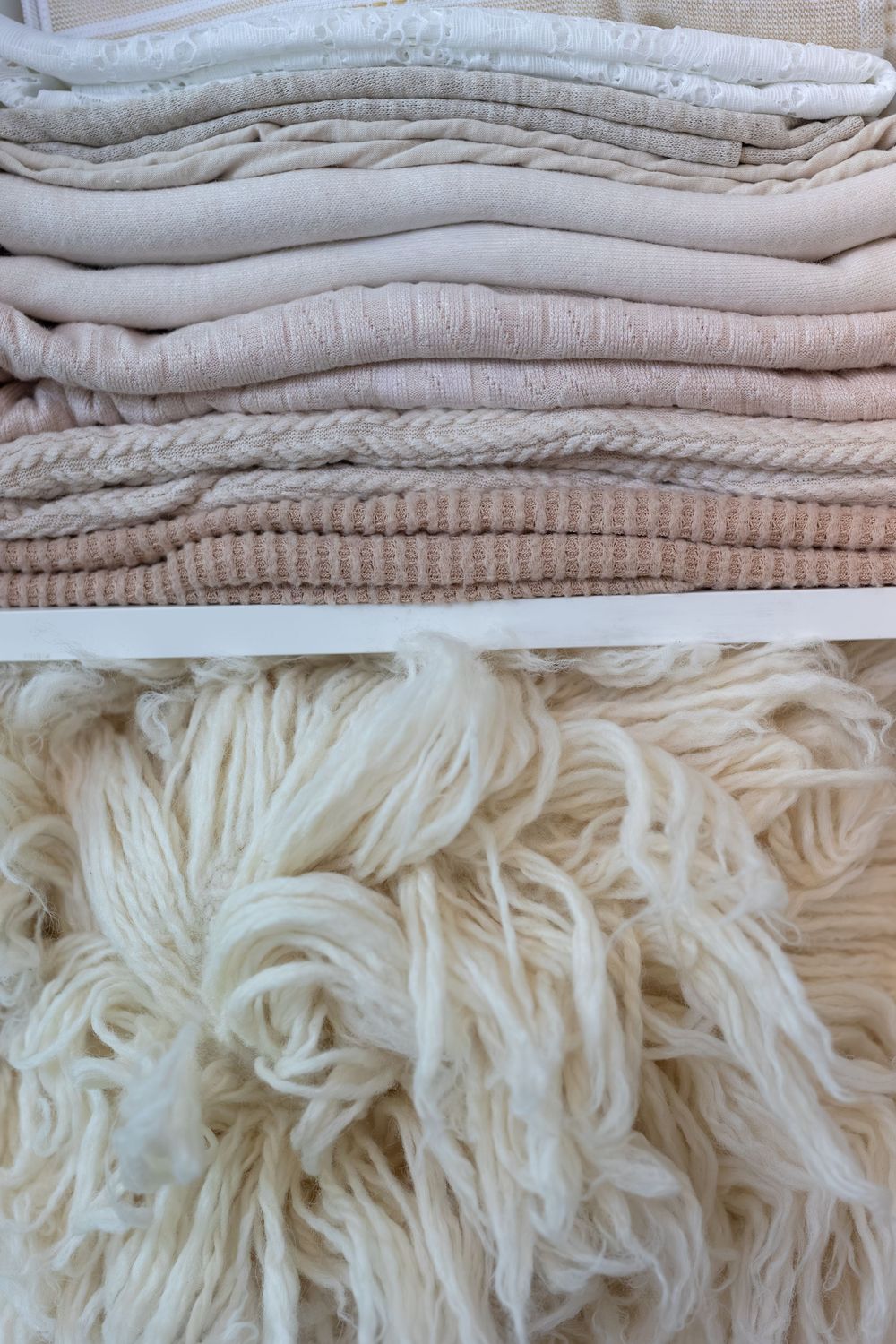 Close-up view of neatly folded white and beige textiles with varying textures and knit patterns stacked together.