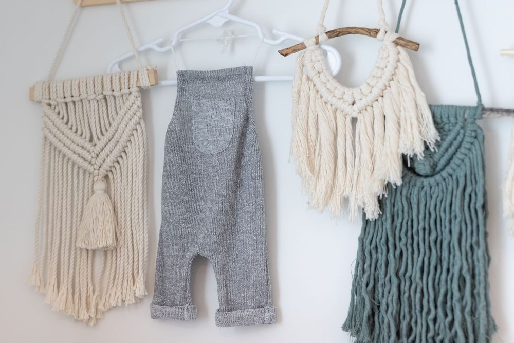 Minimalist baby clothing display with gray leggings and macrame wall hangings in cream and sage green colors.