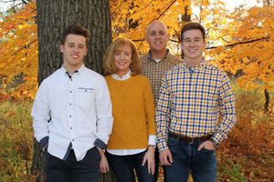 Family of four smiling together outdoors among vibrant autumn foliage with golden and orange leaves.