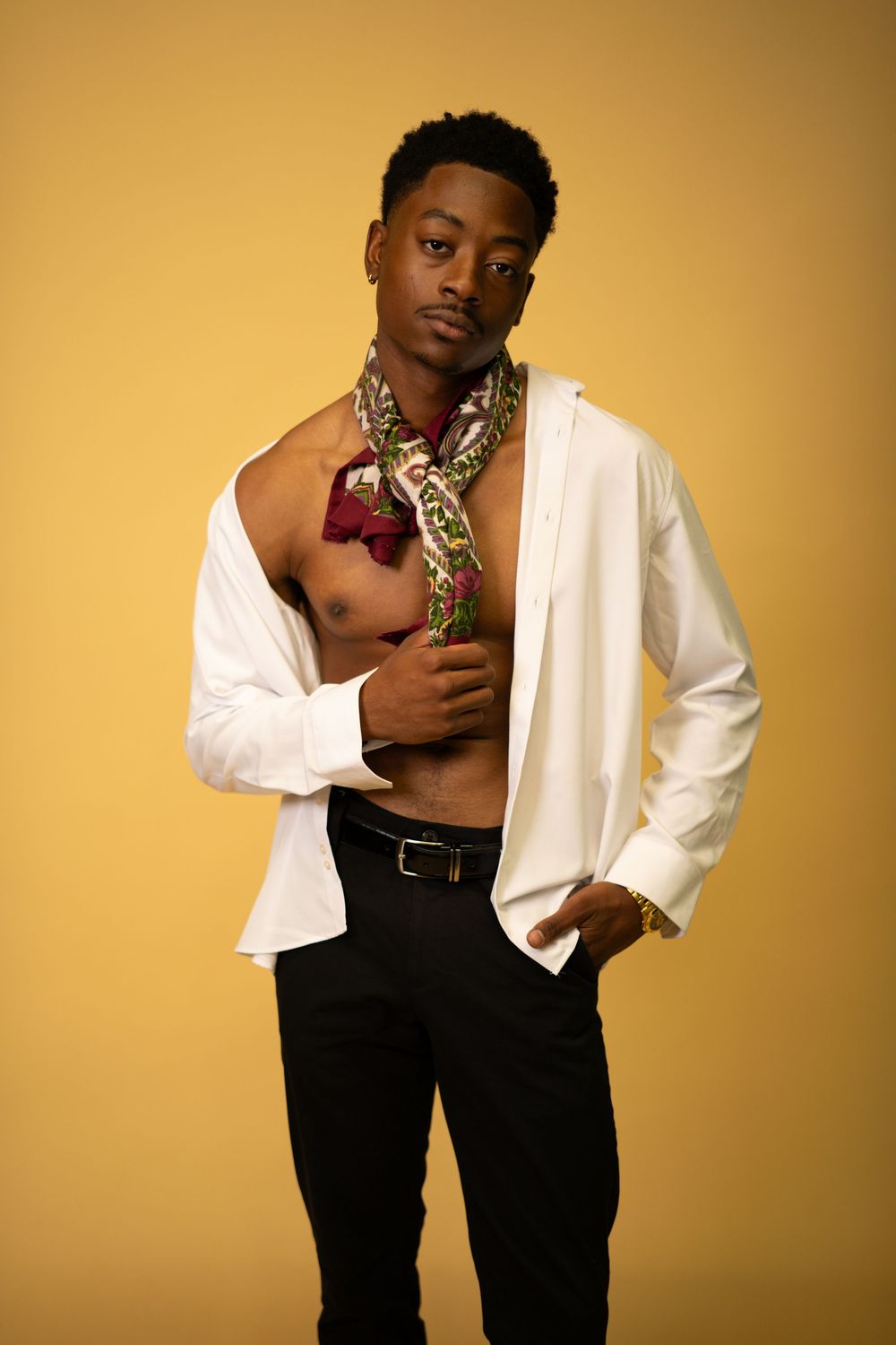 Stylish Black male model in open white shirt with patterned scarf posing on yellow background.
