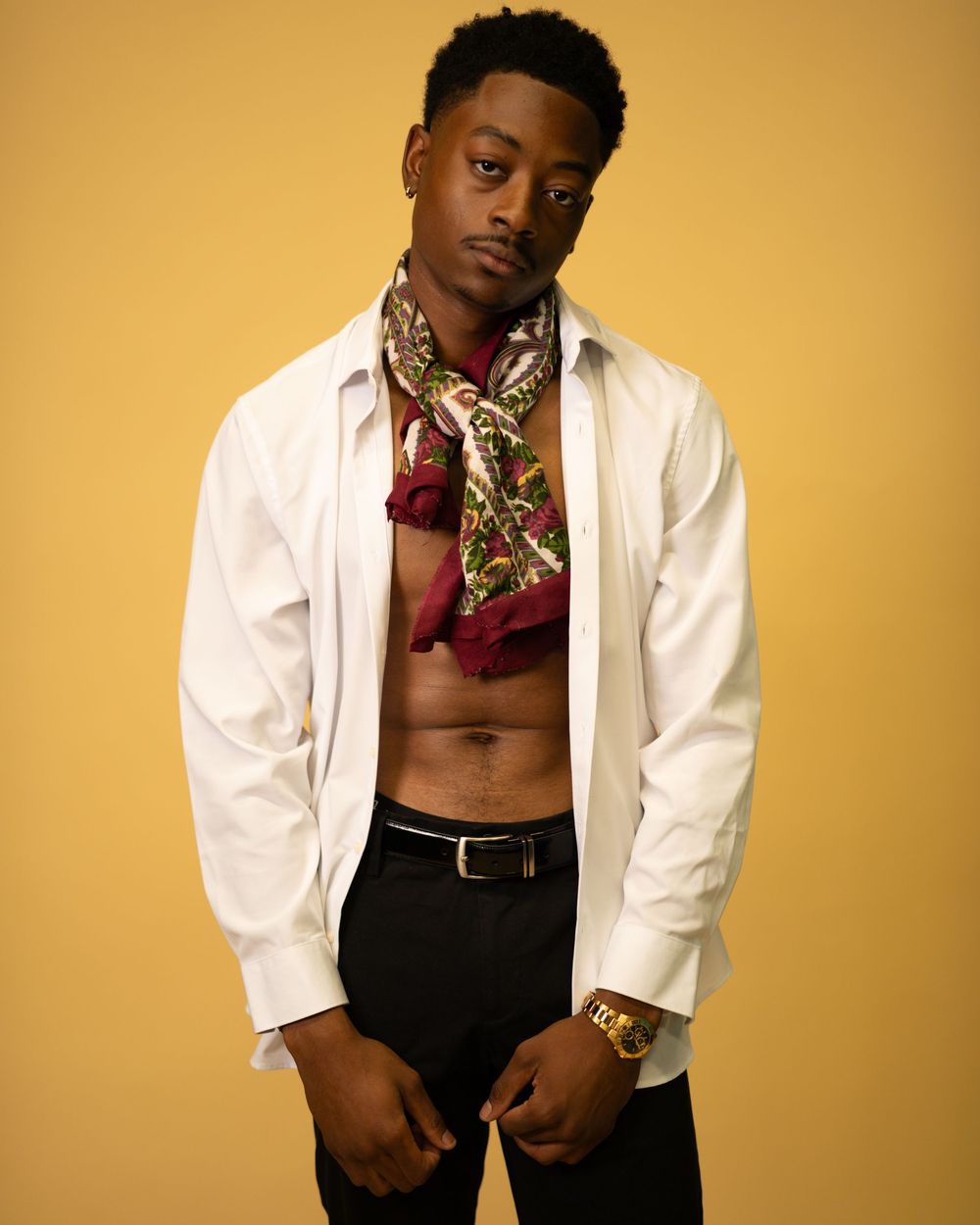Fashionable Black man in open white shirt with patterned scarf on yellow background.
