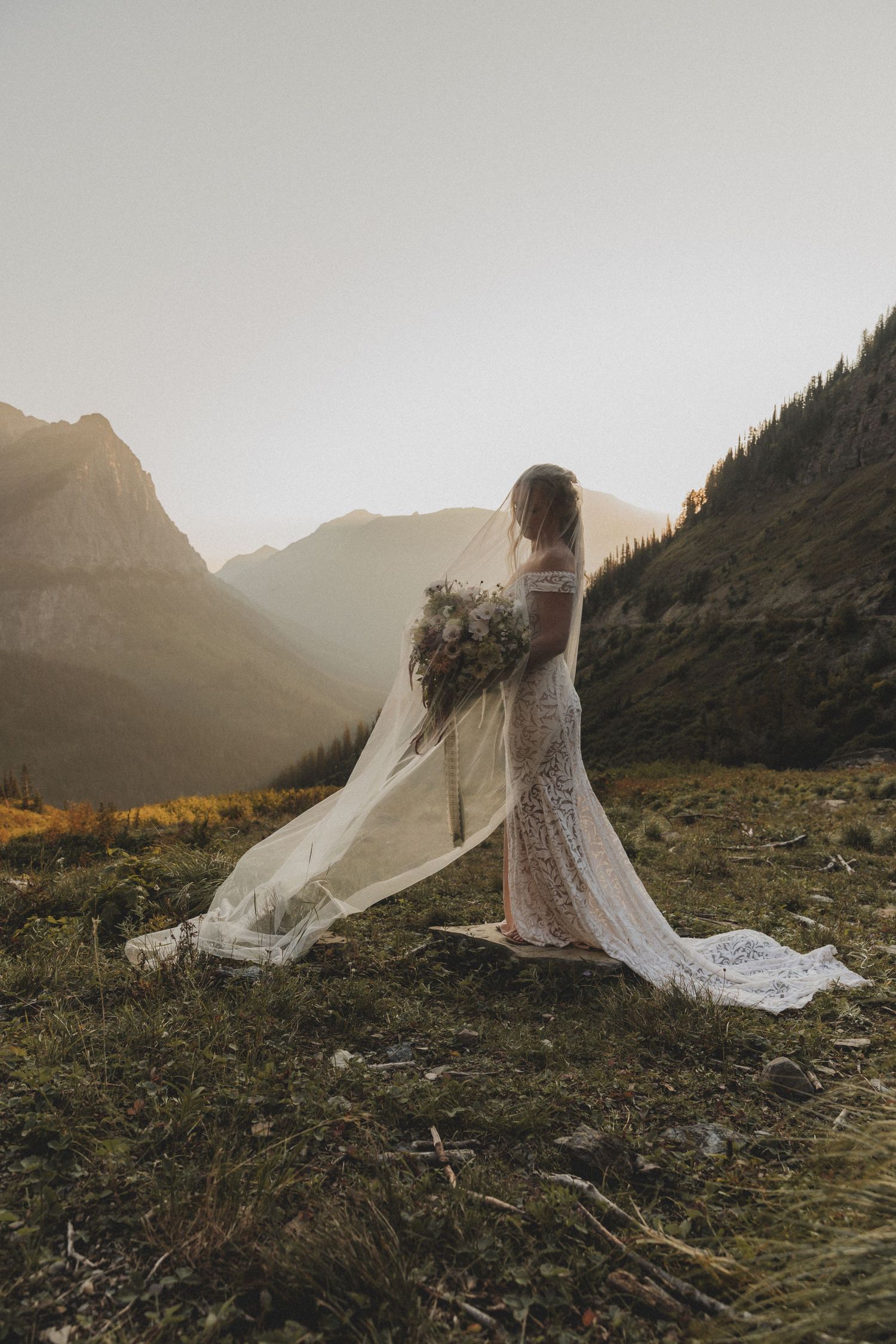 A couple stands at the edge of a misty lake during their outdoor wedding ceremony with a white bouquet.