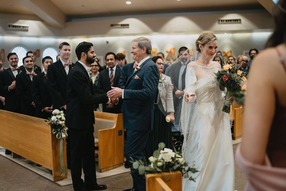 Bride in white gown walks down church aisle with father during traditional wedding ceremony.