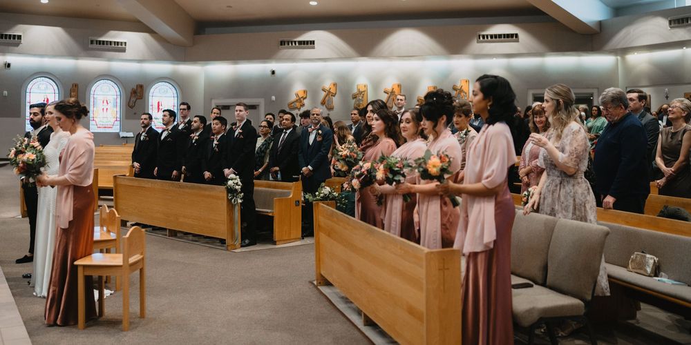 Wedding party stands at altar with bridesmaids in pink dresses holding bouquets during church ceremony.