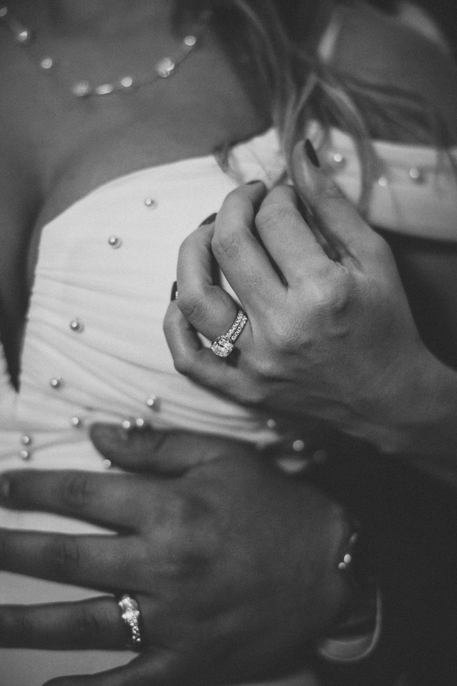 Black and white detail of hands with wedding rings and formal attire.