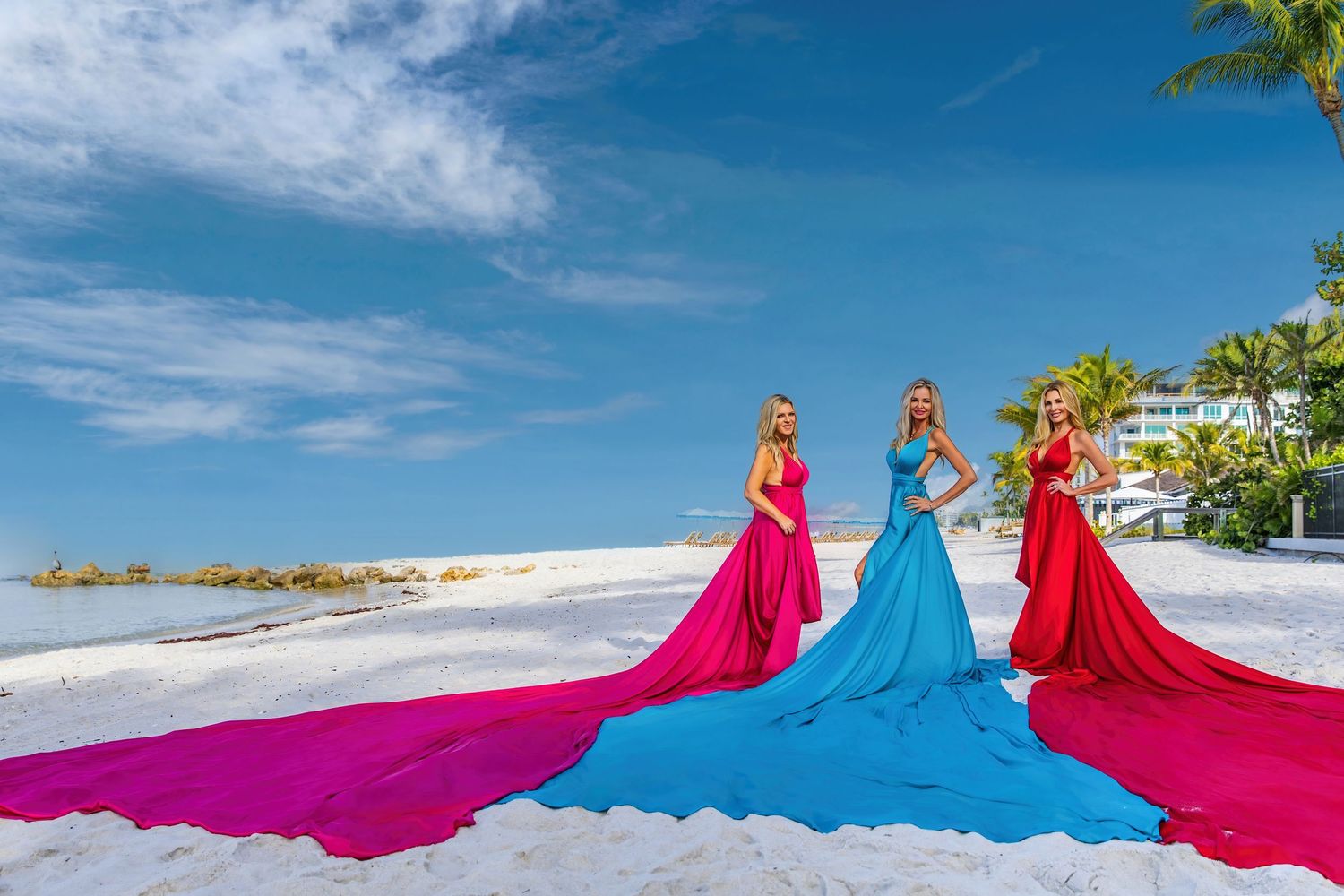 Colorful flowing fabric dresses in pink and blue create a dynamic movement pattern against a beachside backdrop. Flying Dress Photoshoot