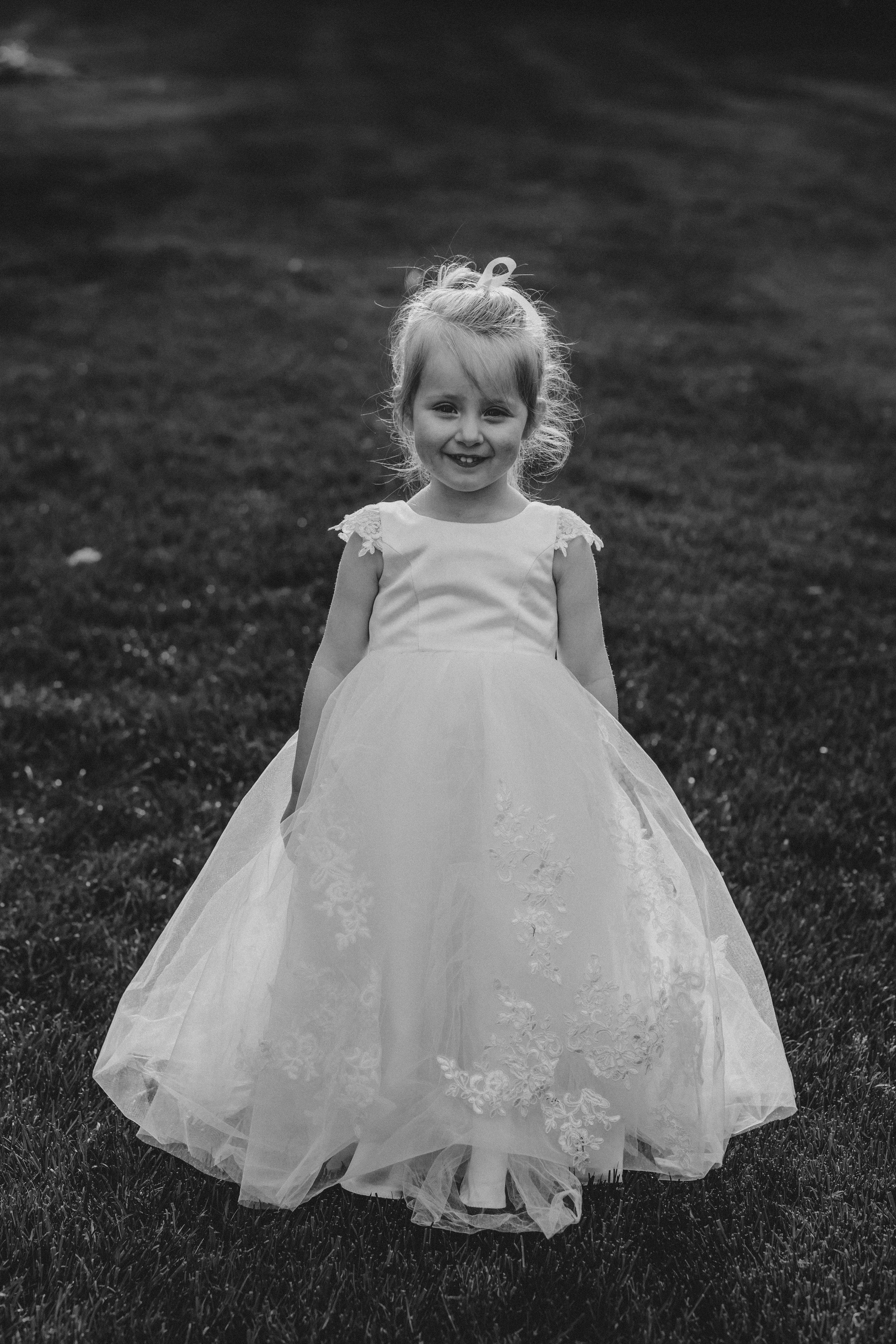 Series of black and white photos showing little girls in white dresses twirling on grass.
