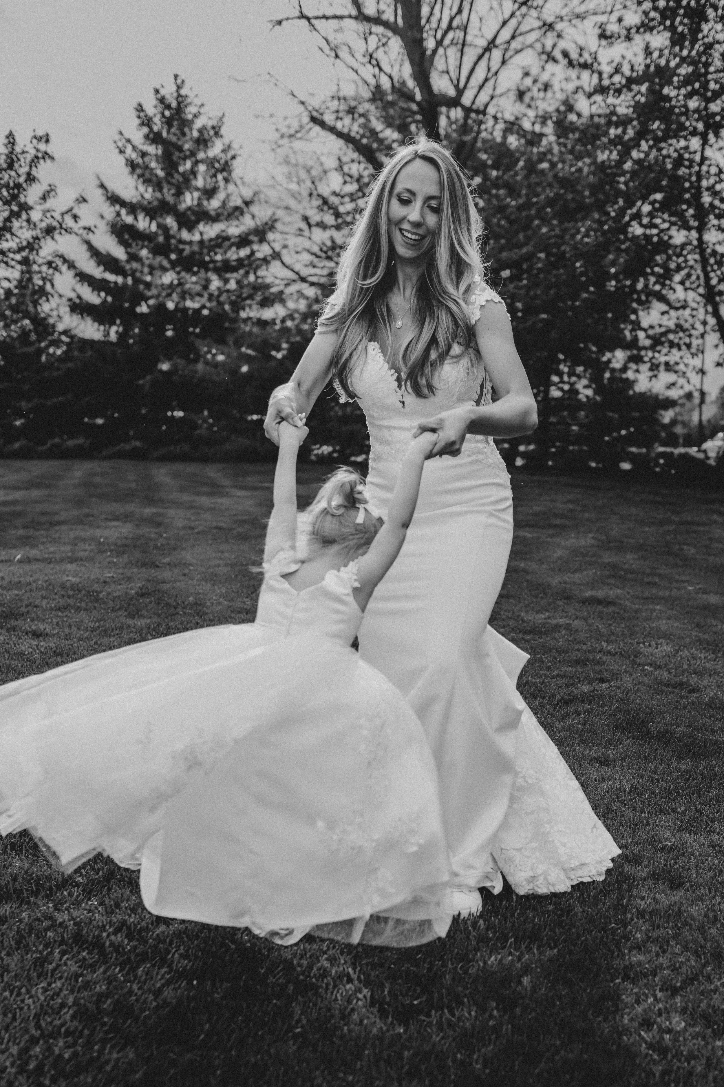 Black and white images capturing playful moments of two people in flowing white dresses dancing on an outdoor lawn.