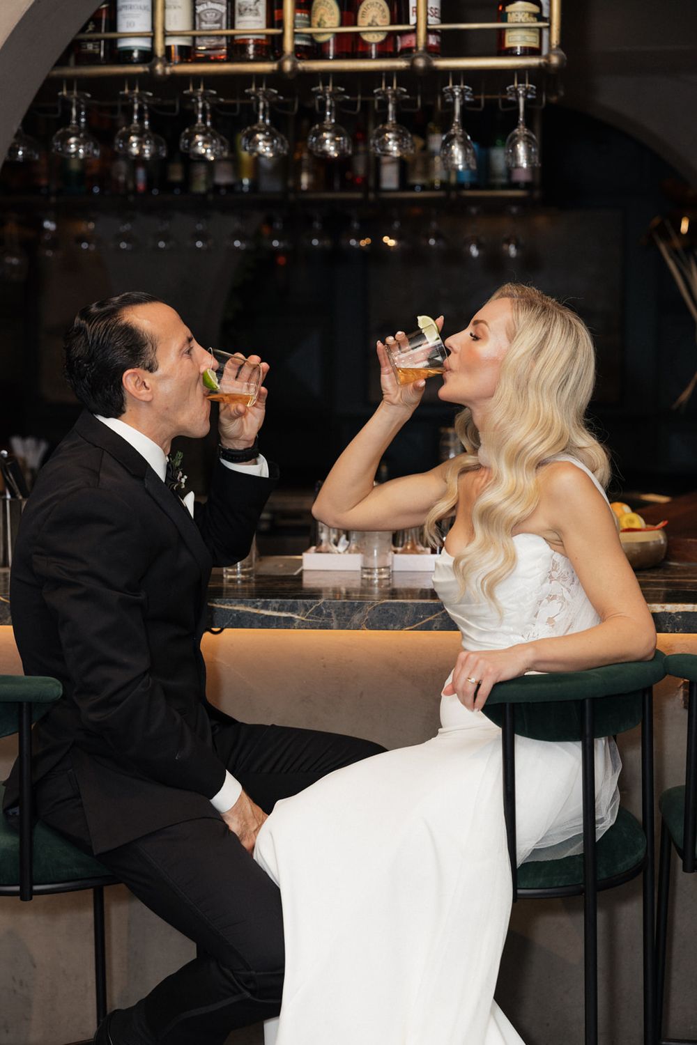 A bride and groom share a playful moment taking shots together at a bar during their wedding reception.