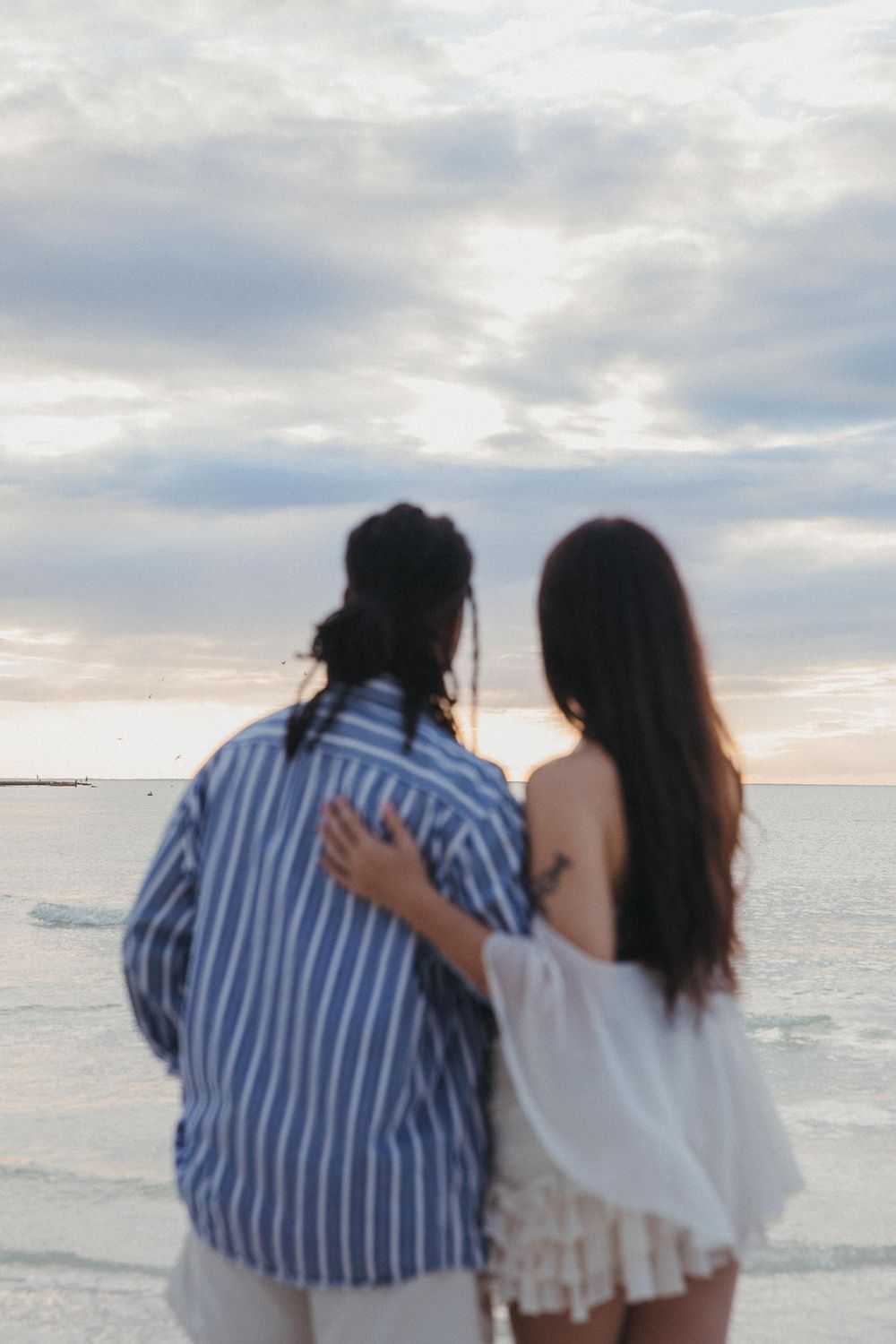 Two woman in white and blue clothing stand together watching a peaceful ocean sunset at the beach in Holbox