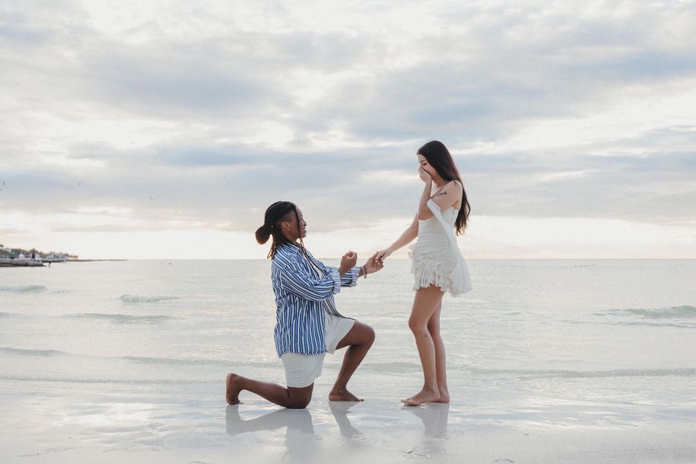 A romantic beach proposal in a classic Holbox scene with two woman on white sand during sunset with cloudy skies in the background.