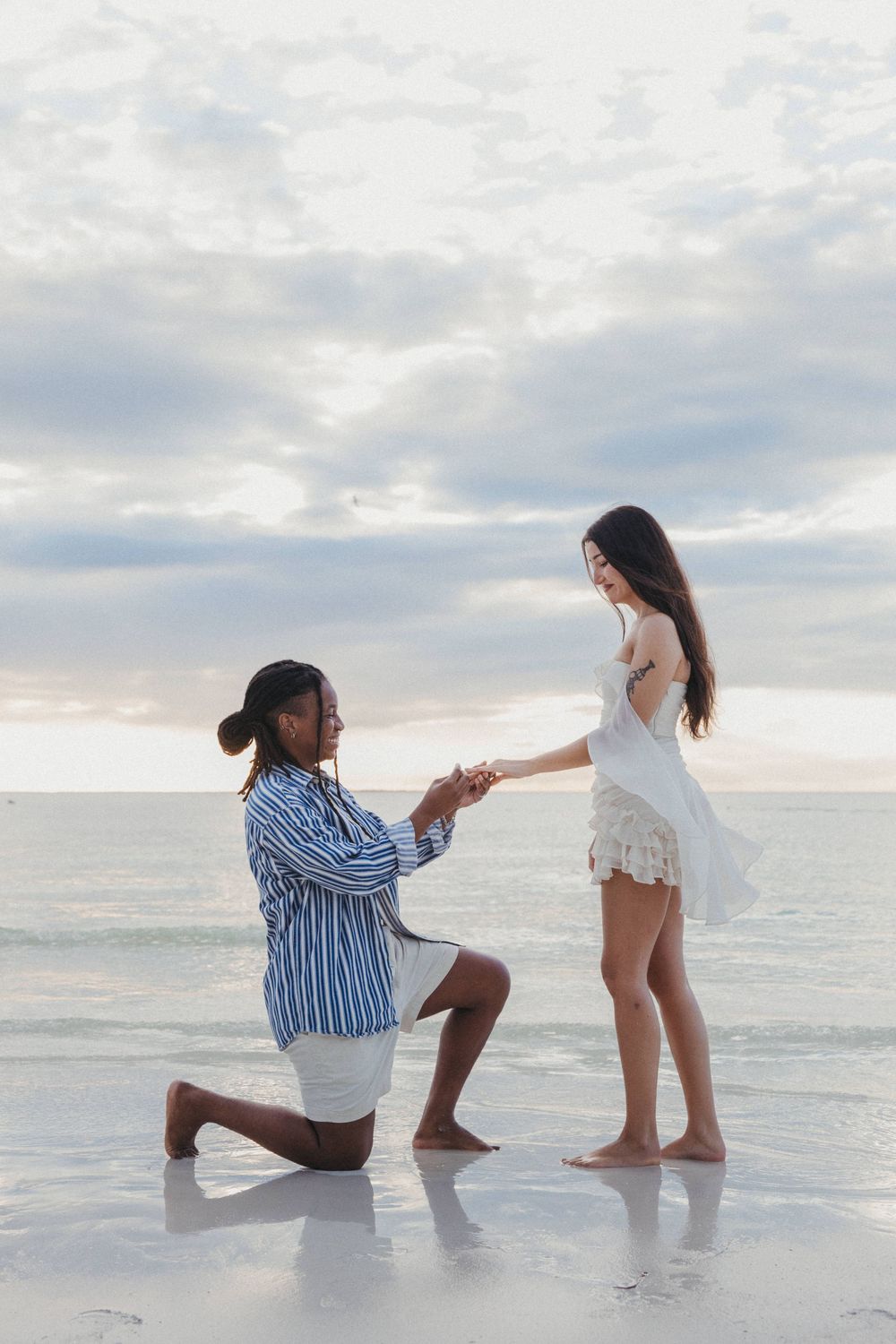 Two people pose playfully together for a surprise proposal on a cloudy beach during a beautiful Holbox sunset.