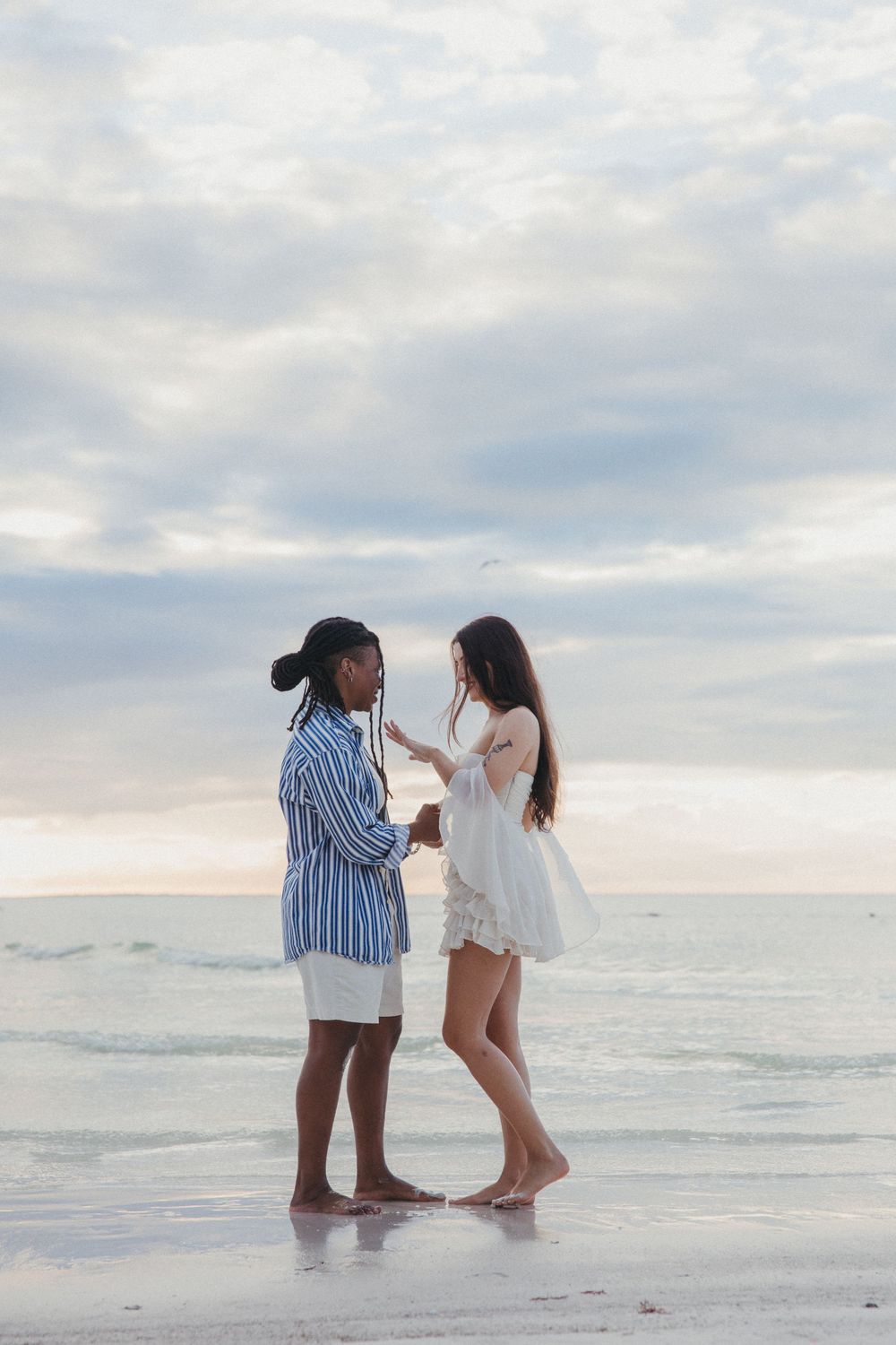 Two people share a surprise proposal moment while standing ankle-deep in ocean waves at sunset on a peaceful beach in Holbox.