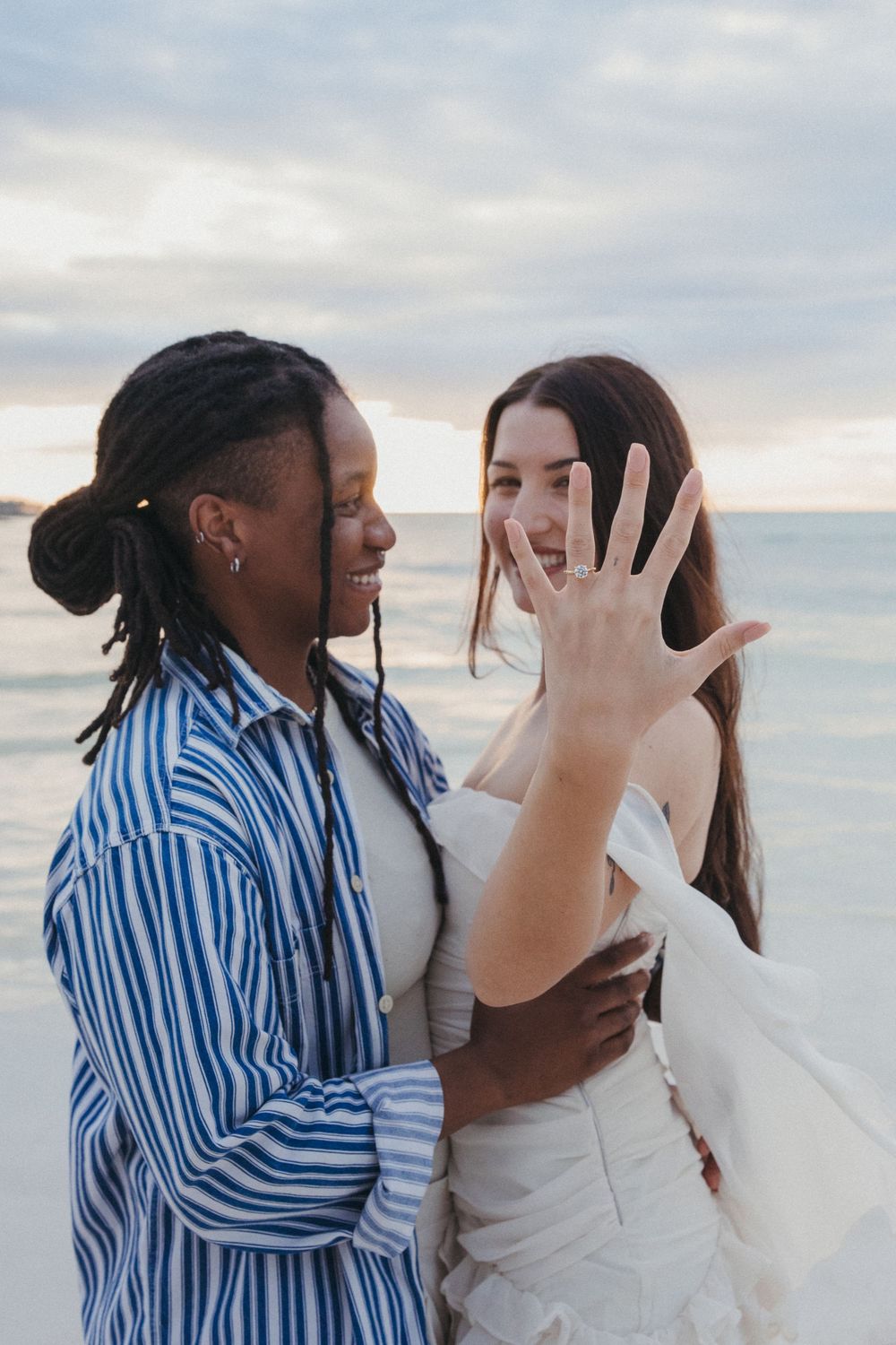 A close-up of a gay interracial couple proudly showing their engagement ring to the camera moments after their sunset proposal in Holbox.