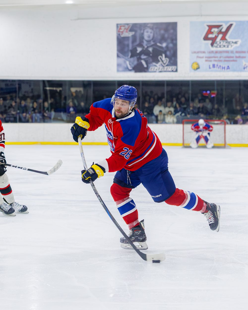 Lumsden Monarchs number 26 player shoots the puck during a fast-paced competitive ice hockey game.