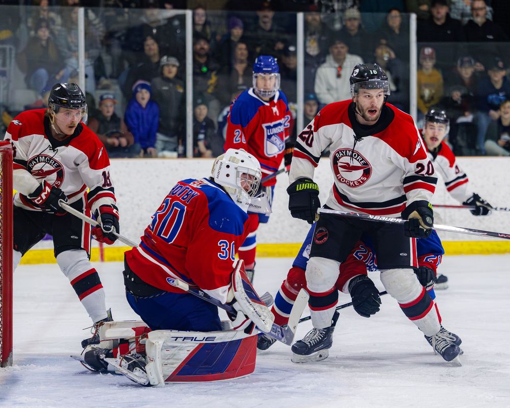 Hockey goalie number 30 in red makes a save during intense game action with players battling nearby.