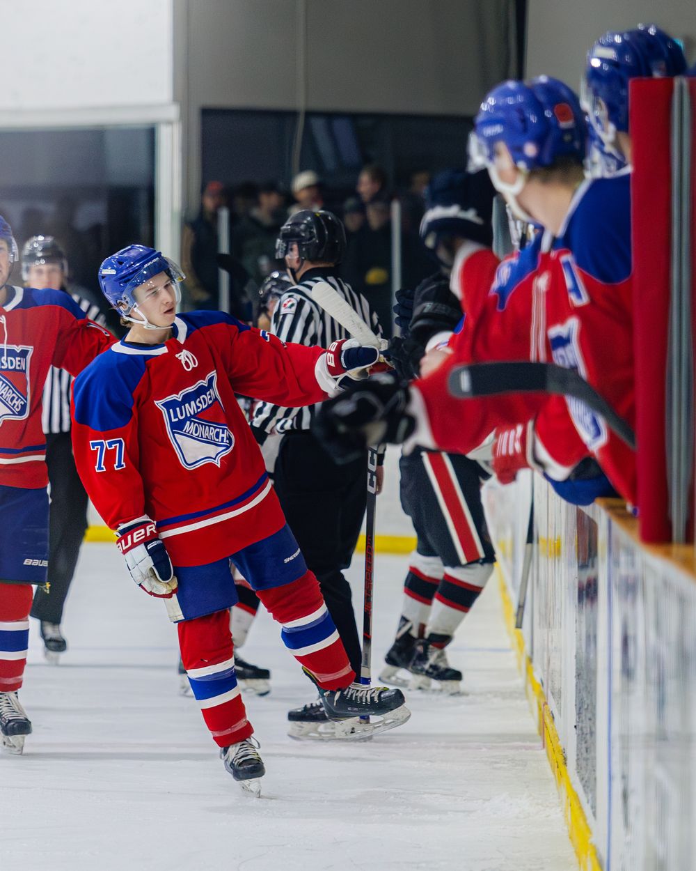 Hockey player number 77 in red jersey high-fives teammates at the bench after scoring a goal.