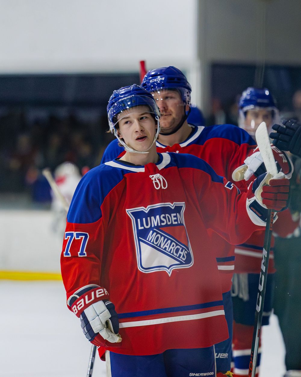 Two Lumsden Monarchs hockey players including number 77 stand together on ice during a game.