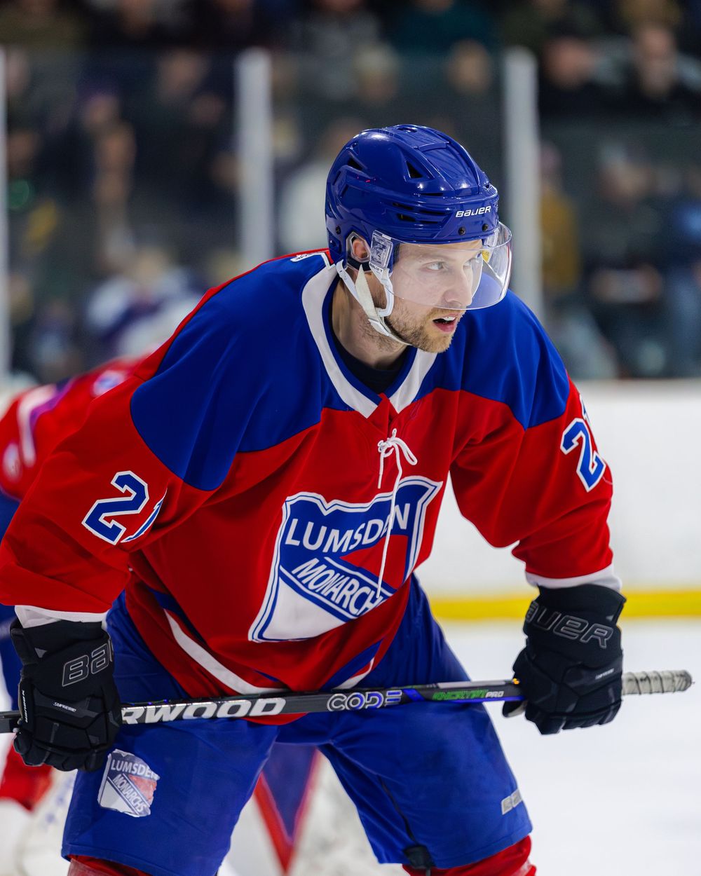 Lumsden Monarchs number 21 player in red and blue jersey skates focused during a hockey game.