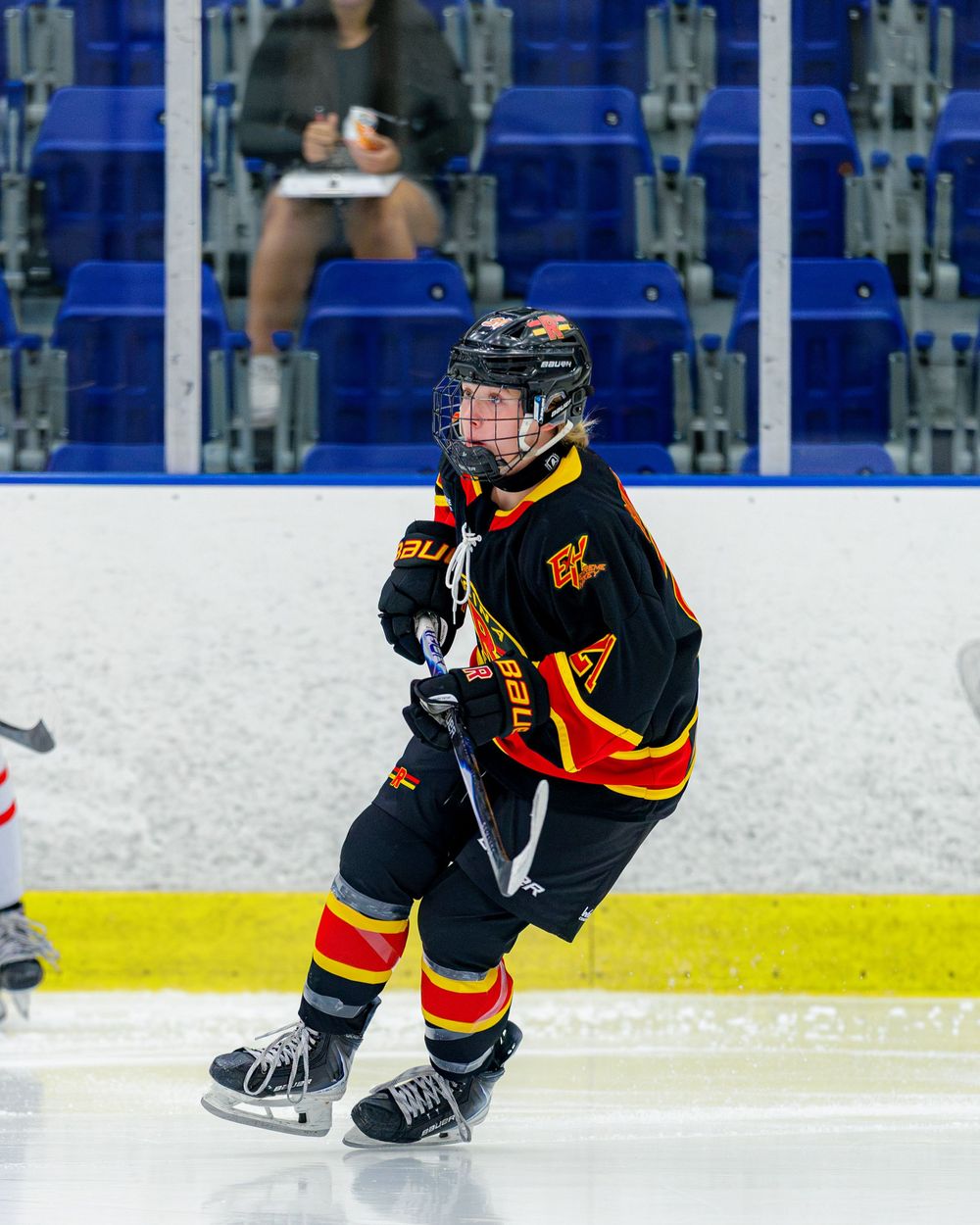 Young ice hockey player in black and yellow uniform skating on indoor rink during a game.