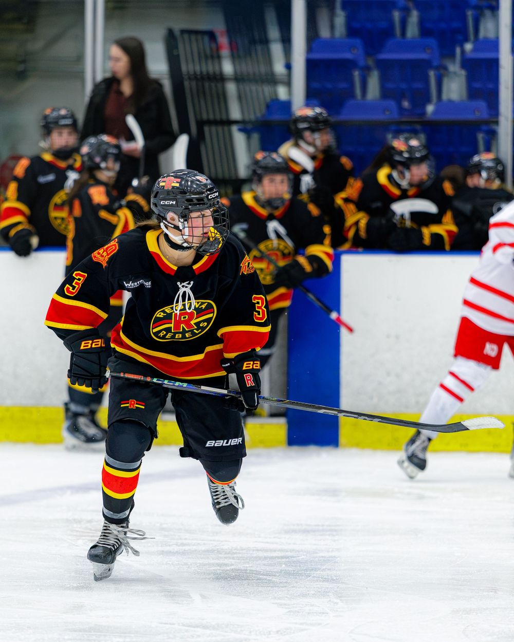 Youth hockey player wearing black and yellow jersey number 3 skating on ice during a competitive game.