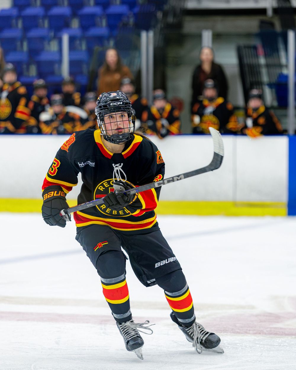 Hockey player in black Rebels jersey skating on ice during a game.
