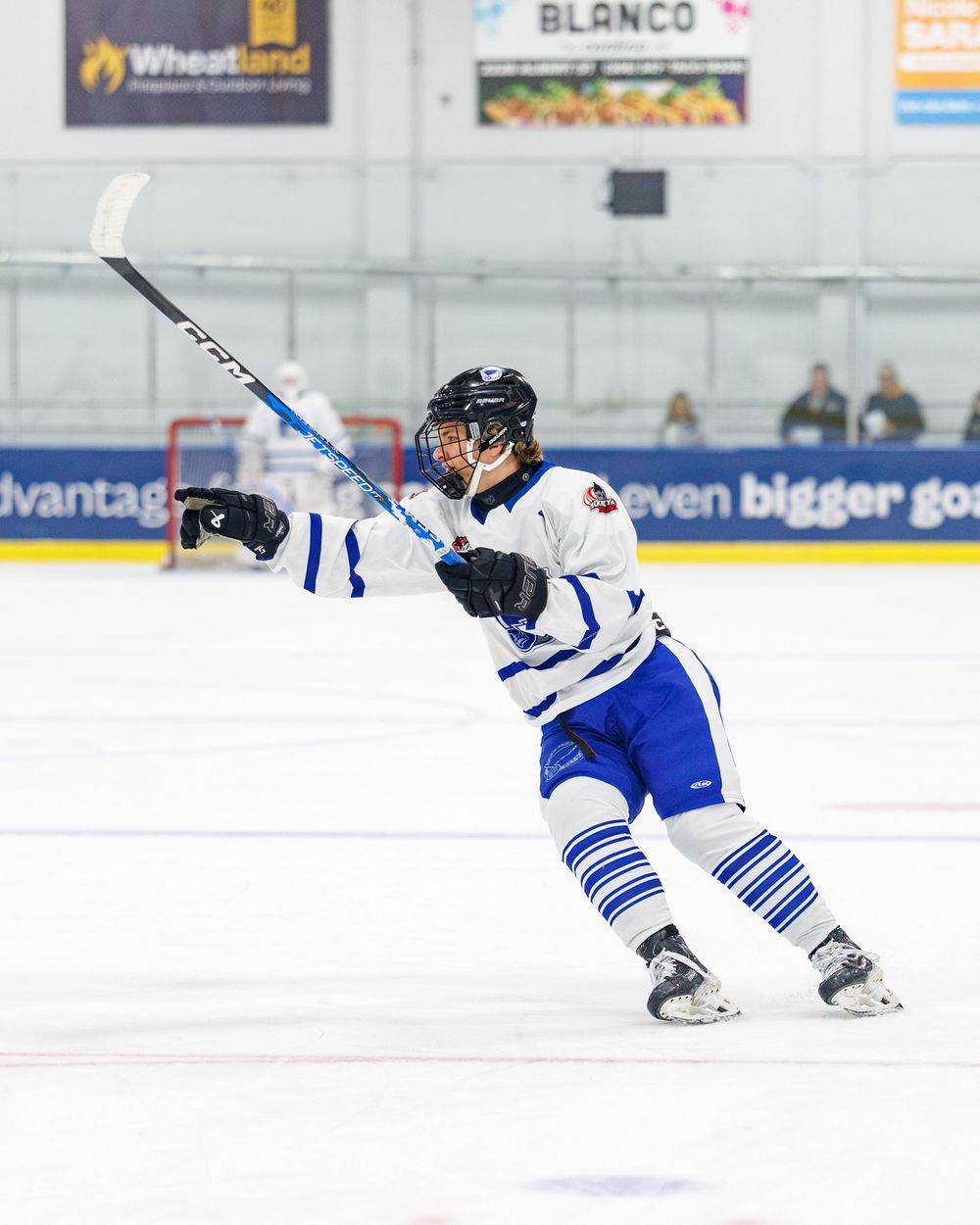 Hockey player in white and blue uniform takes a shot on ice rink during competitive game.
