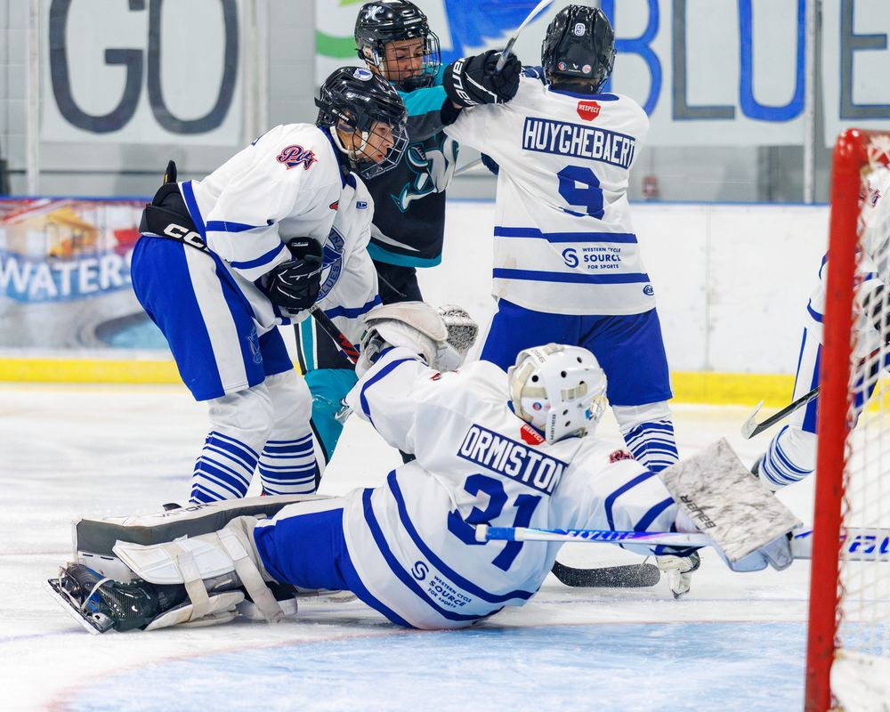 Hockey players in blue and white uniforms battle near the goal during an intense ice hockey game.