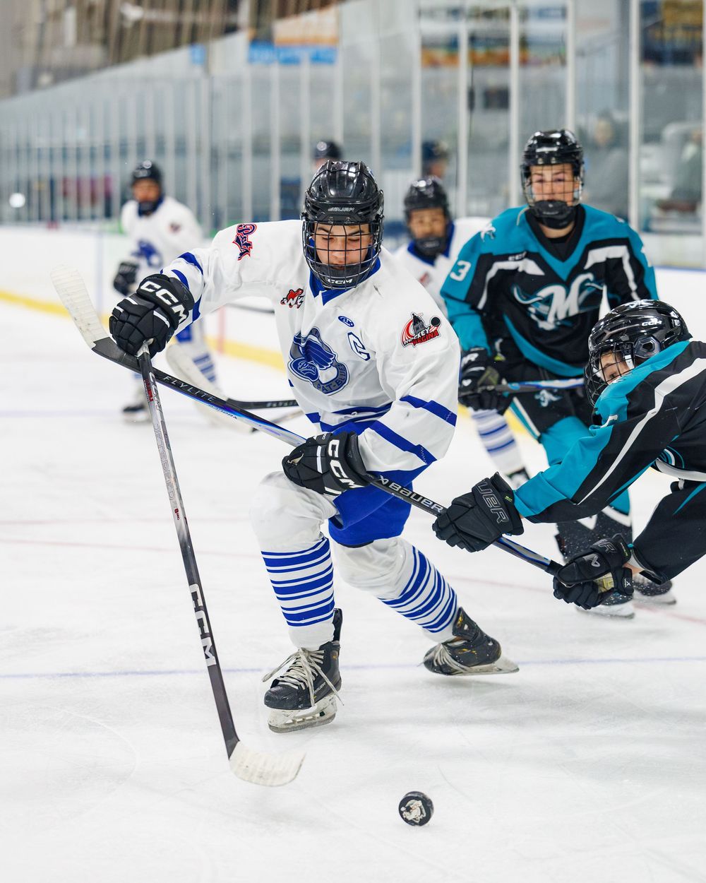 Youth ice hockey player in white and blue uniform skating with puck during competitive game.