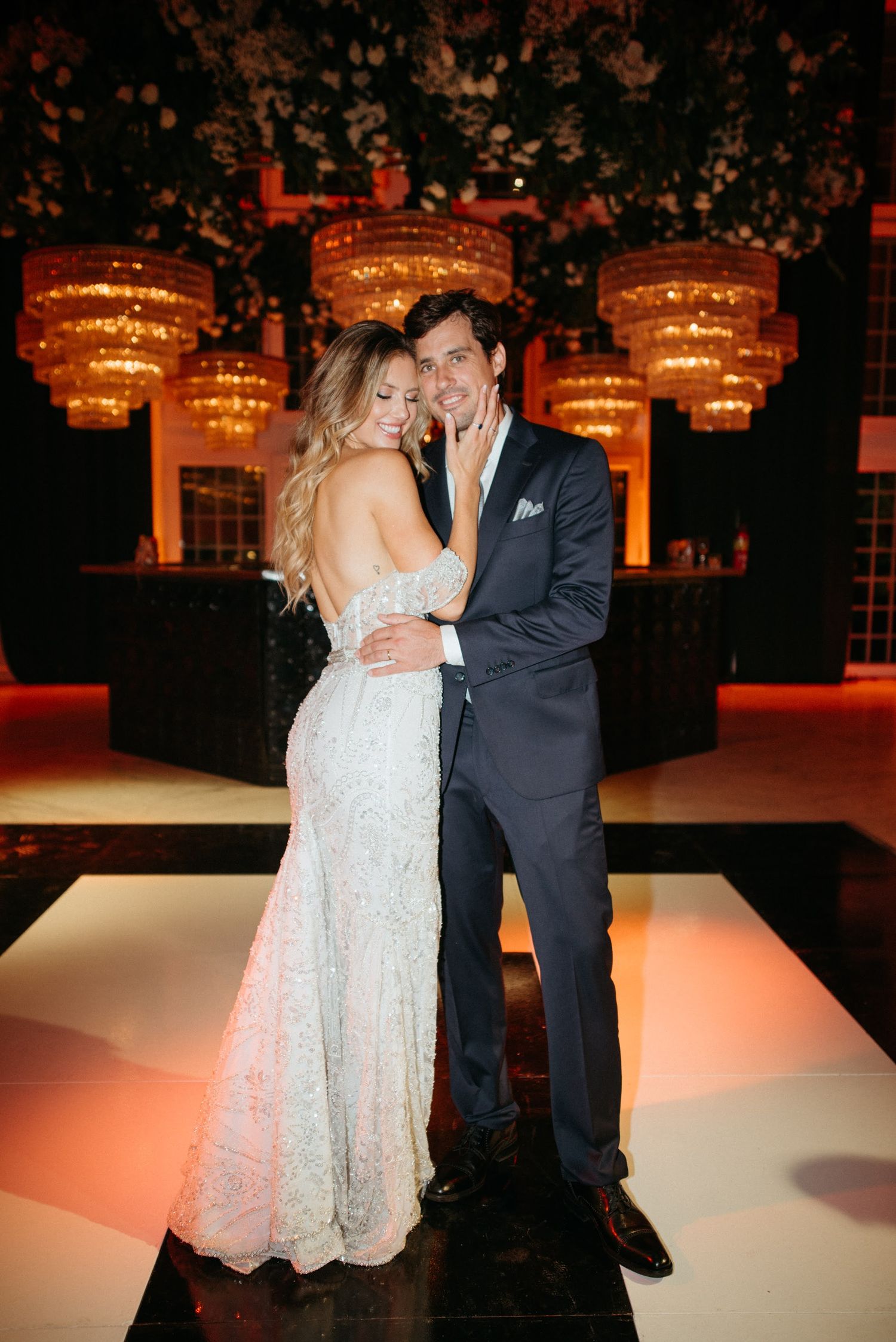 A couple shares a romantic dance together at their wedding reception on an illuminated white dance floor.