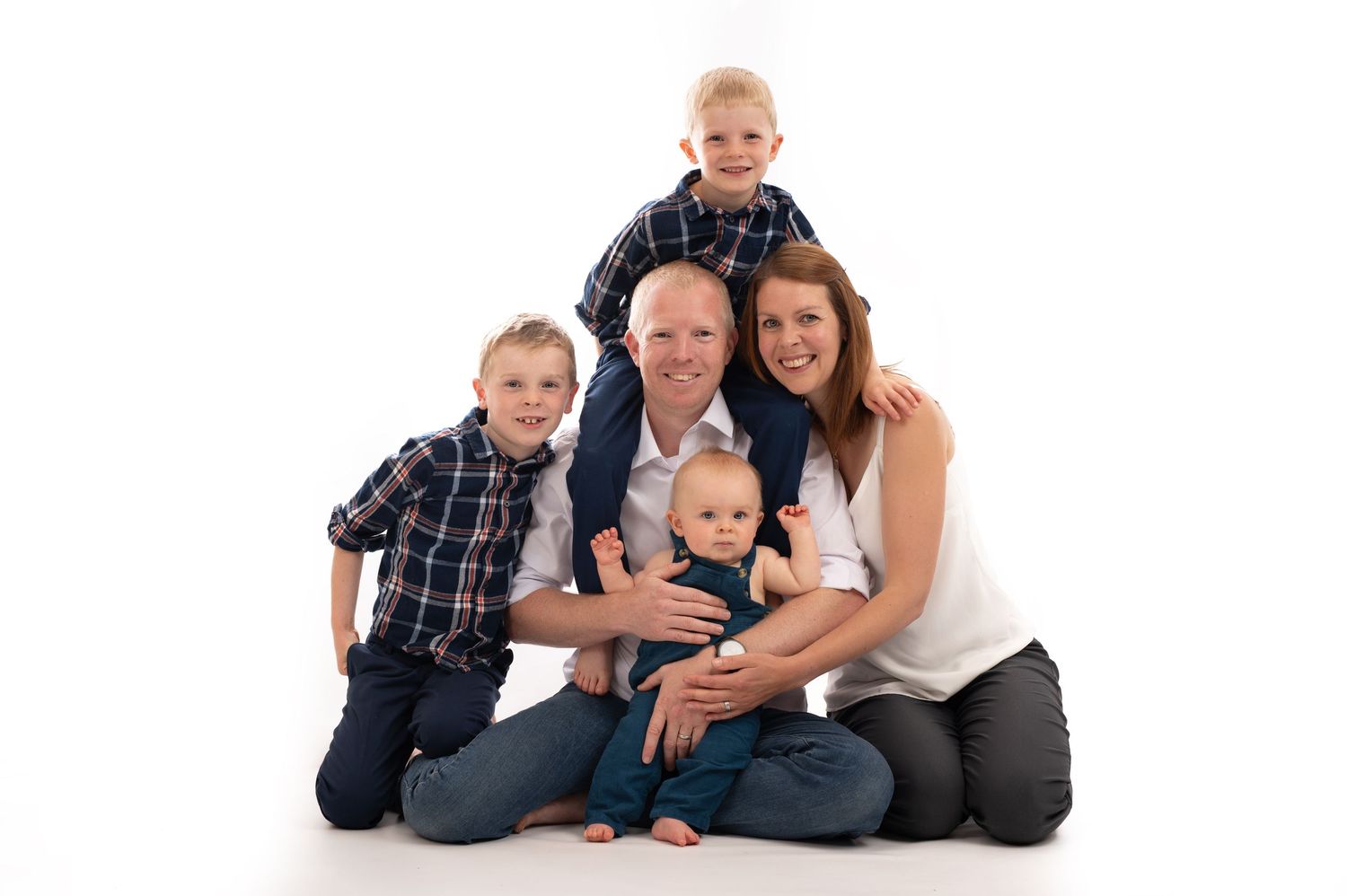 Family wearing coordinating blue and white outfits poses together on white backdrop for professional portrait session.